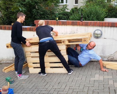 Mitarbeiter bauen gemeinsam Palettenmöbel beim Teambuilding-Event