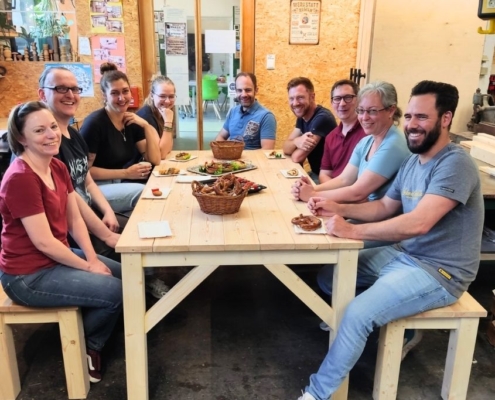 Firmenteam sitzt gemeinsam an selbstgebautem Holztisch nach Schreiner-Workshop