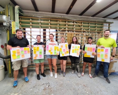 Team hält bunte Ideen-Plakate nach Kreativphase im Schreiner-Workshop